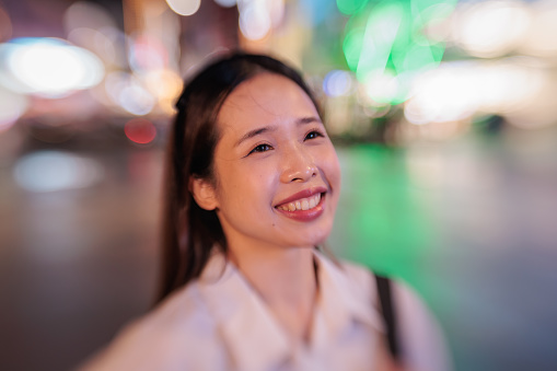 Portrait of a young woman looking into the distance and smiling in the city at night.