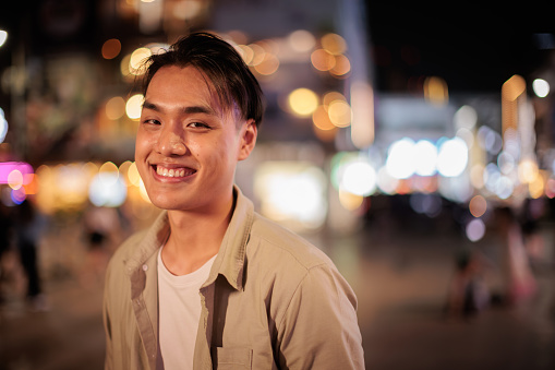 Portrait of a young man looking at the camera and smiling in the city at night.