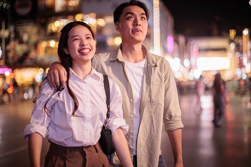 A smiling couple is walking embraced in the city at night.