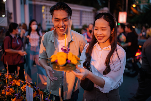 A smiling couple is buying krathong from a market stall on night of the Loy Krathong festival.