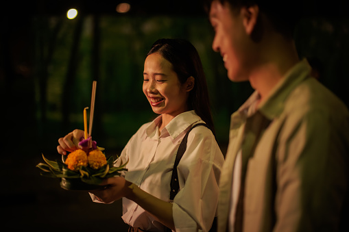 Smiling couple is walking with krathong in hands, on night of the Loy Krathong festival.