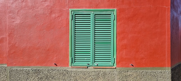 A green closed shutter on a red wall on a sunny day