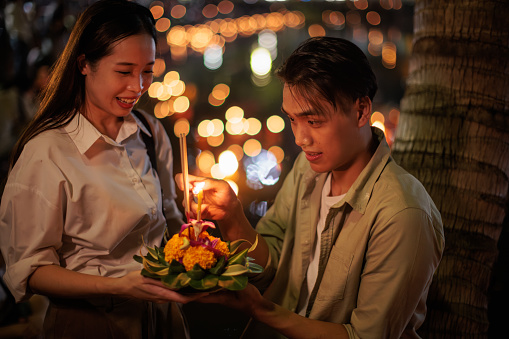 A smiling couple holds a krathong by the river during the Loy Krathong festival night.