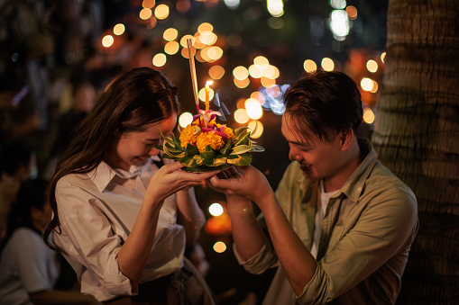 A smiling couple is praying with a krathong to honor the Water Goddess at Loy Krathong festival night.
