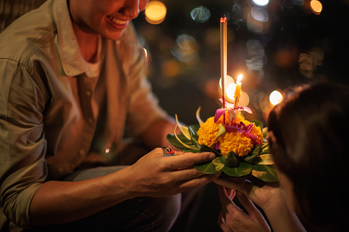 Midsection of a couple holding a krathong by the river during the Loy Krathong festival night.