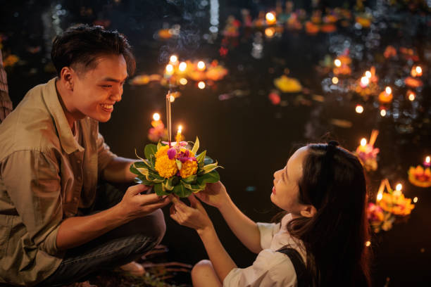 Couple at the Loy Krathong festival A smiling couple holds a krathong by the river during the Loy Krathong festival night. krathong stock pictures, royalty-free photos & images