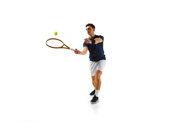 Competitive man in his 30s, tennis player in motion, hitting ball with racket, practicing isolated over white background. Concept of professional sport, competition, game, math, hobby, action