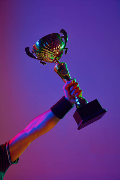 istock Male hand holding trophy against gradient studio background on neon light. Winner, champion, success 1909095499