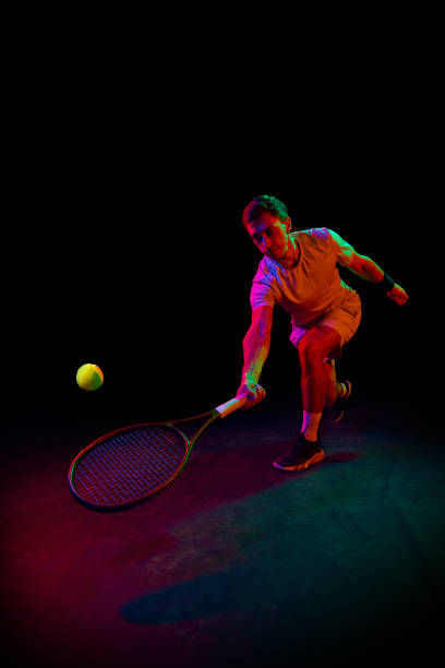 istock Young man, tennis player during game, playing, practicing against dark background in neon light 1909095503