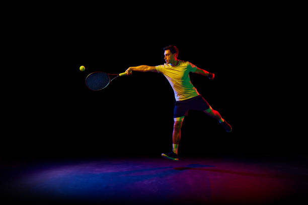 istock Concentrated and competitive man, tennis athlete during training session, hitting ball with racket against dark background in neon light 1909095508