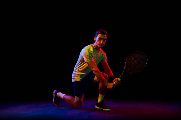 istock Concentrated athletic man, tennis player in motion, training, practicing against dark background in neon light 1909095517