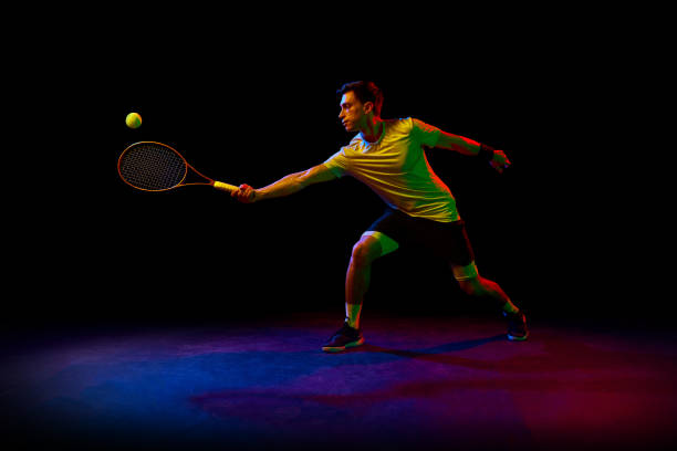 istock Concentrated and competitive man, tennis athlete during training session, hitting ball with racket against dark background in neon light 1909095518