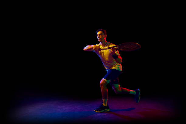 istock Concentrated athletic man, tennis player in motion, training, practicing against dark background in neon light 1909095519