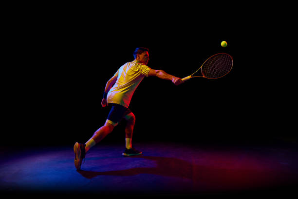 istock Concentrated and competitive man, tennis athlete during training session, hitting ball with racket against dark background in neon light 1909095520