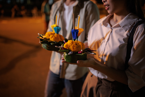 Midsection if a couple walking with krathongs in hands, on night of the Loy Krathong festival.