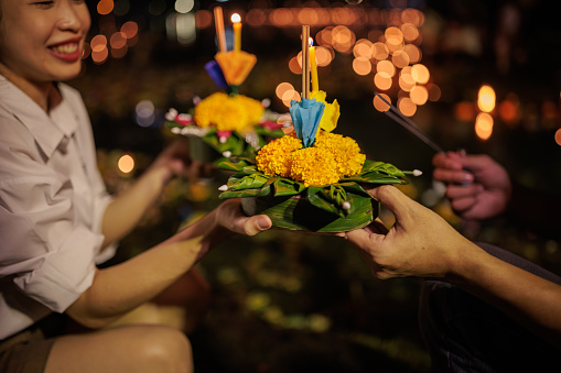Midsection of a couple holding a krathong by the river during the Loy Krathong festival night.