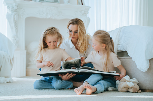 Attentive mother reading a book with her two young daughters on the floor, fostering a love for reading in a cozy, light-filled room