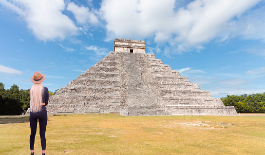 Yucatan, Mexico - November 05, 2023:  Girl tourist in a hat stands against the background of the pyramid of Kukulcan in the Mexican city of Chichen Itza - Mayan pyramids in Yucatan, Mexico
