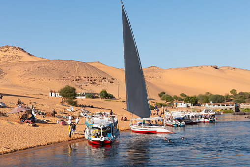 Aswan, Egypt - Decemebr 14 2023: Navigating the Nile River, several tour boats waiting for tourists near a Nubian town.