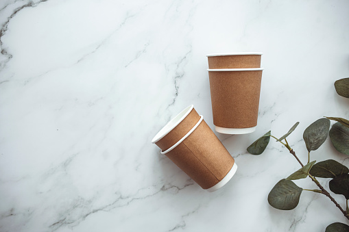Set of disposable coffee nug and table ware, eco friendly. Disposable cardboard cup with empty space for text on gray background. Take out coffee or delivery service. Copy space.