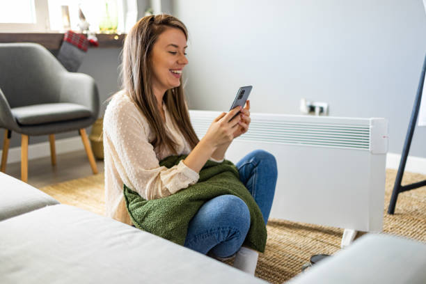 istock Woman and radiator using smartphone app for temperature control 1909149472