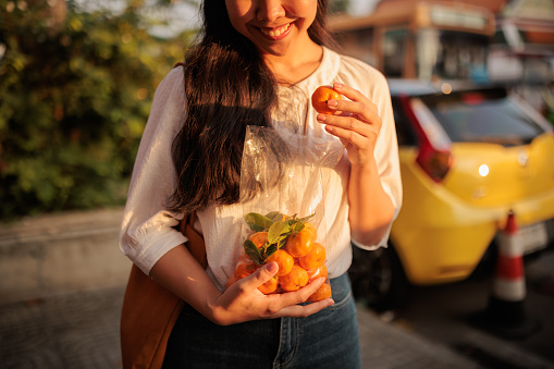 The midsection of a smiling woman holding a bag of oranges.
