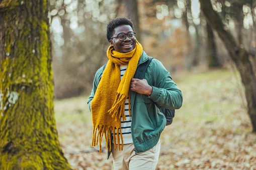 A young man of African-American nationality in glasses with a backpack on a walk in the woods to his location. Active people and the concept of travel.