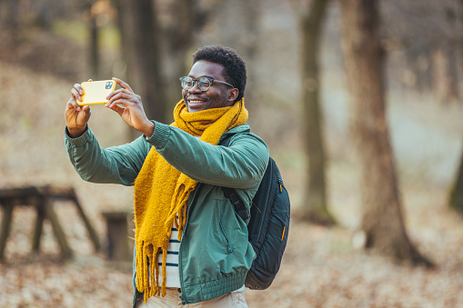 A cheerful African-American enjoys taking selfies. Travel alone, explore wildlife, stay positive. Camping in the woods, time for adventure and the concept of rest