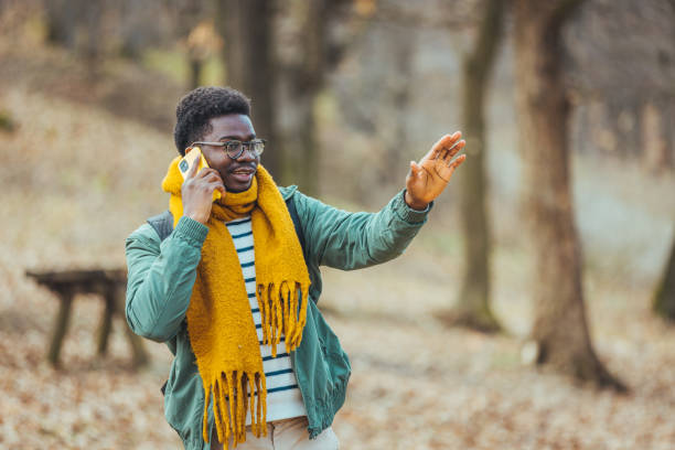 A positive young manwalking in the mountains talks on the phone with a smile on his face and points his finger to the side. The concept of peace and distance