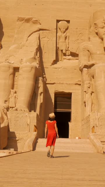 A young woman in a red dress walking towards the temple of nefertari next to the temple of Abu Simbel in southern Egypt in Nubia next to Lake Nasser. Temple of Pharaoh Ramses II, 4k video