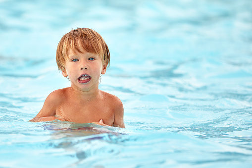 Little boy in the pool with a displeased face, surprised kid in the water of the pool, copy space