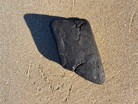 A piece of coal on sand background at coastline beach
