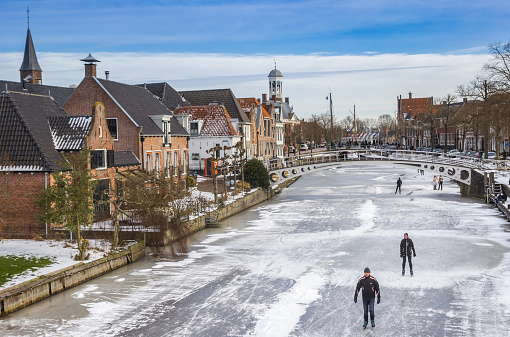 People skating on ice on the Thorbeckegracht in Zwolle, The Netherlands during a beautiful winter day. Ice skating is a popular winter sport and leisure activity in The Netherlands.