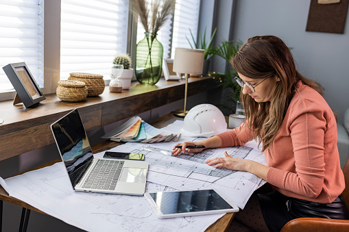 Shot of a young businesswoman working with blueprints in an office. Shot of an attractive young architect working in her office. Female architect working at home. She looking at blueprint