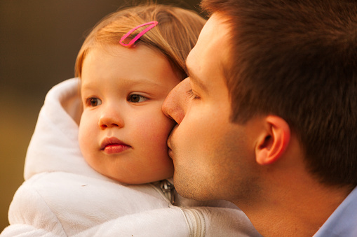 With a gentle kiss on the cheek, the father cherishes a quiet moment with his contemplative young daughter