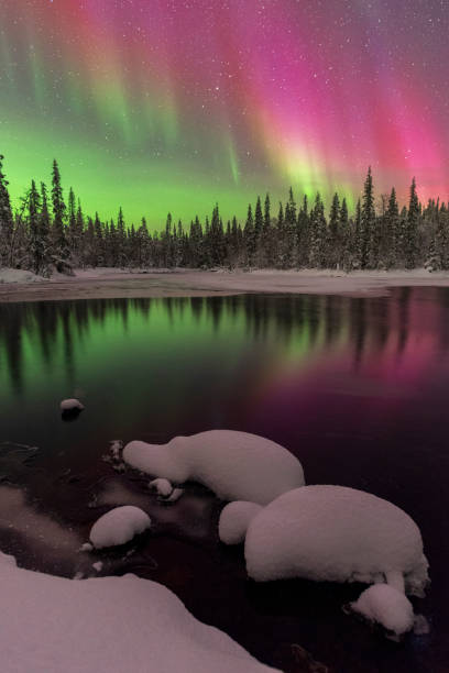 Colourful northern lights and the reflection in the lake, Finland Winter night view with geomagnetic storm above the arctic sky showing northern lights with green and red colors reflecting in the water of a lake covered with snow and ice, Lapland, Finland, Scandinavia mirror lake stock pictures, royalty-free photos & images