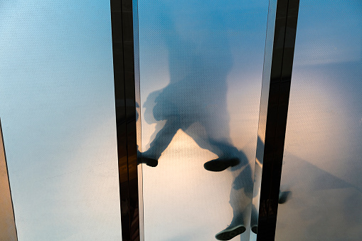 Shadows and feet of people on glass floor, low angle view.
