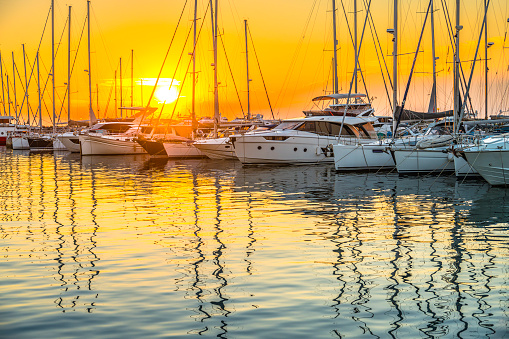Embracing the idyllic sunset in Istria,Croatia,a carefree woman stands with her arm outstretched on the silhouette of a sailboat in the enchanting seascape. The scene captures the serene beauty of the Adriatic coast,where the sun sets in hues of warmth