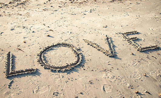 Sun protect factor. SPF word written on the sand and white bottle with suntan cream. Skin care concept background.