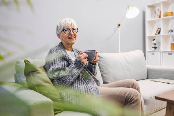 istock Beautiful 50 years old caucasian lady sit down on the sofa drinking tea 1909323573
