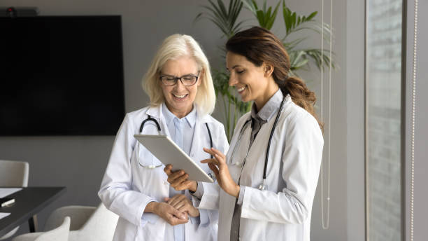 istock Two positive young and senior doctor women using tablet together 1909325573