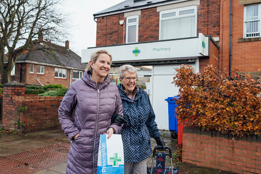 A mature woman out and about with her mother in Seghill, Northumberland. The senior woman has dementia and is arm in arm with her daughter for support and assistance as they walk on a footpath in town. They have just picked up the senior woman's prescription at the pharmacy behind them.

Videos also available for similar scenario.