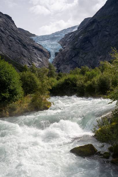 istock Rocky range and glacier with green trees and a river in the foreground. Briksdalsbreen, Norway 1909458343