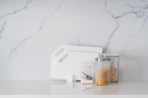 Kitchen utensils, cutting boards, knives, cooking ingredients and kitchenware on white modern kitchen table with marble background