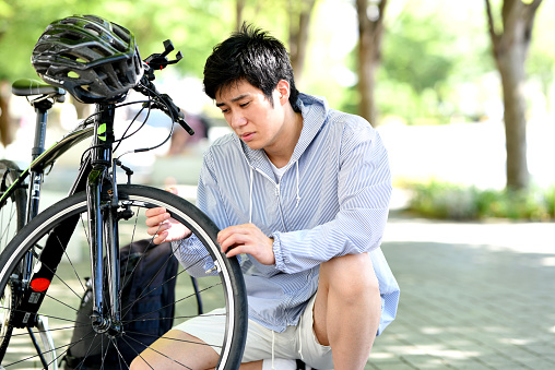 Young Asian man suffering from bicycle trouble outdoors