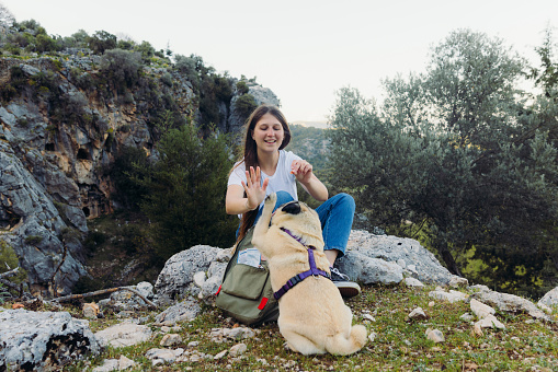 Happy female with backpack relaxing after hike in the woodland with her dog and playing with him for treats in Pinara, Lycia, South Turkey