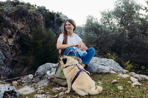 Happy female with backpack relaxing after hike in the woodland with her dog and playing with him for treats in Pinara, Lycia, South Turkey