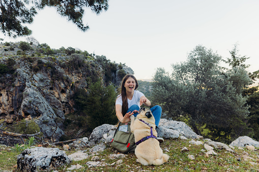 Happy female with backpack relaxing after hike in the woodland with her dog and playing with him for treats in Pinara, Lycia, South Turkey