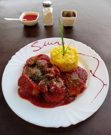 Bolivian pork dish Mondongo. The meat is stewed in a sweet paprika sauce served alongside two starches, potatoes and corn.