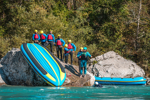 A rafting team's bonding is on full display as they creatively use their raft to slide down by the river, showcasing the spirited side of their journey.